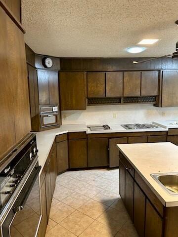 kitchen featuring dark brown cabinetry, wall oven, light countertops, a textured ceiling, and a sink