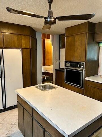 kitchen with a ceiling fan, freestanding refrigerator, wall oven, light countertops, and a sink