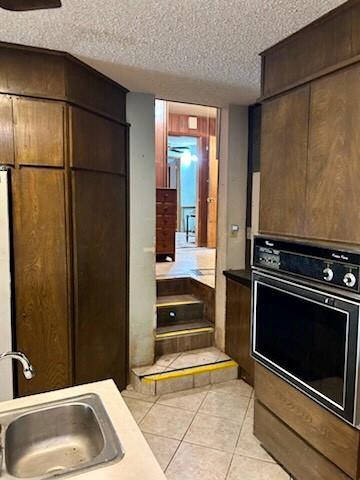 8 Burk Way, Del City, OK 73115 - kitchen featuring black oven, a sink, light tile patterned floors, a textured ceiling, and dark brown cabinetry