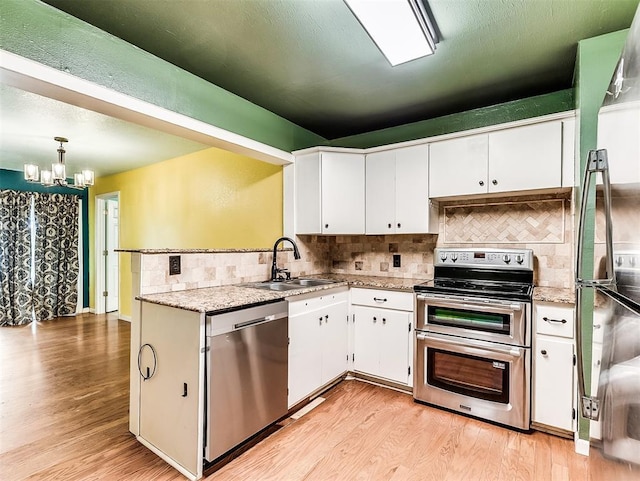 kitchen with light wood-style floors, appliances with stainless steel finishes, a sink, an inviting chandelier, and white cabinetry