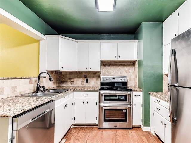 kitchen featuring stainless steel appliances, tasteful backsplash, a sink, and light wood-type flooring