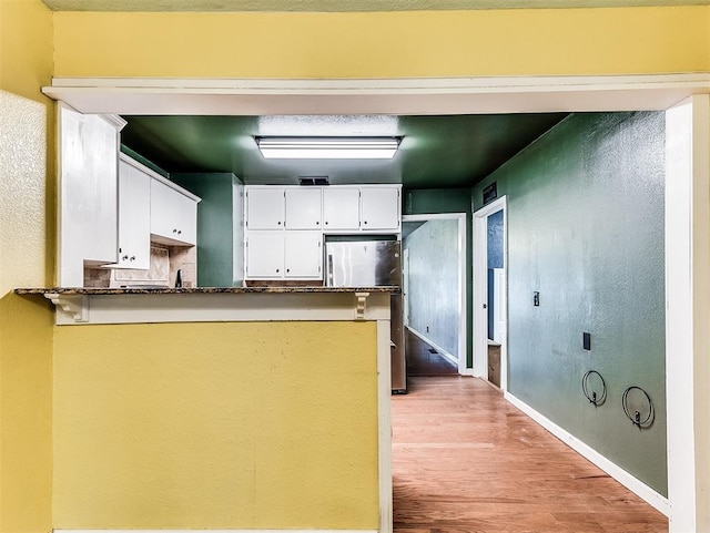kitchen featuring freestanding refrigerator, a peninsula, light wood-style floors, baseboards, and white cabinetry