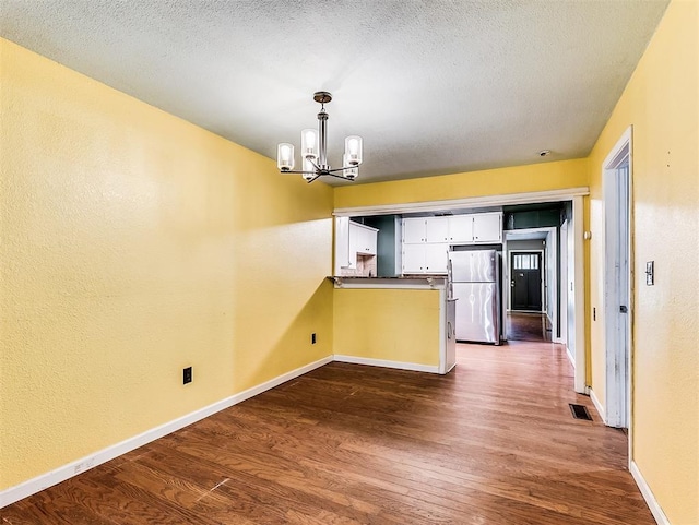 unfurnished dining area with a notable chandelier, a textured ceiling, baseboards, visible vents, and dark wood-style floors
