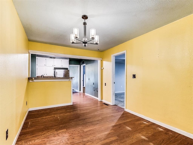 unfurnished dining area with baseboards, a notable chandelier, and dark wood finished floors
