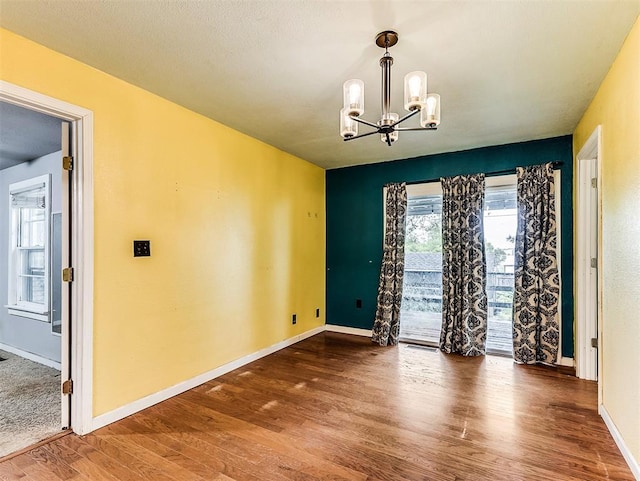 empty room with baseboards, wood finished floors, and a notable chandelier