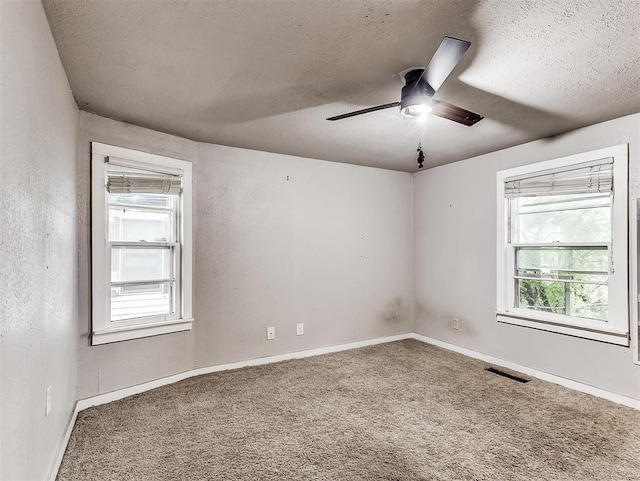 carpeted empty room featuring visible vents, a ceiling fan, a textured ceiling, and a wealth of natural light
