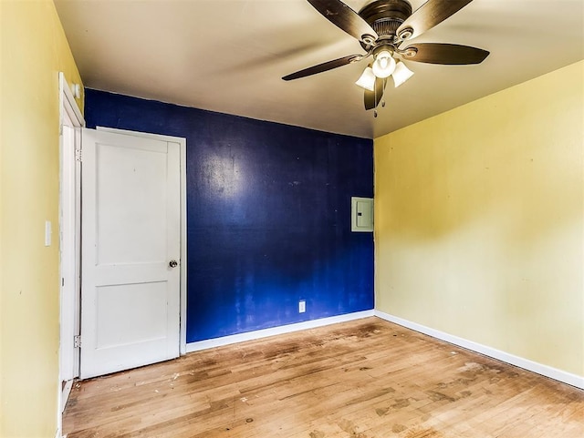 empty room featuring a ceiling fan, baseboards, wood finished floors, and electric panel