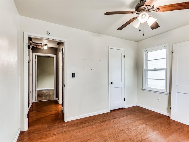 unfurnished bedroom featuring baseboards, ceiling fan, attic access, and wood finished floors