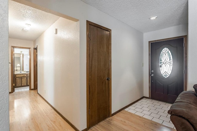 foyer with light wood-type flooring, a textured ceiling, and baseboards