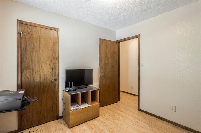bedroom featuring baseboards, light wood-type flooring, and a textured ceiling