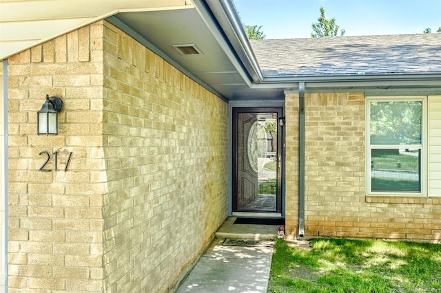 entrance to property featuring brick siding and a shingled roof