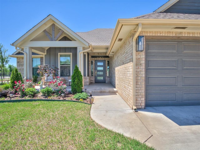doorway to property with board and batten siding, roof with shingles, a lawn, a garage, and brick siding