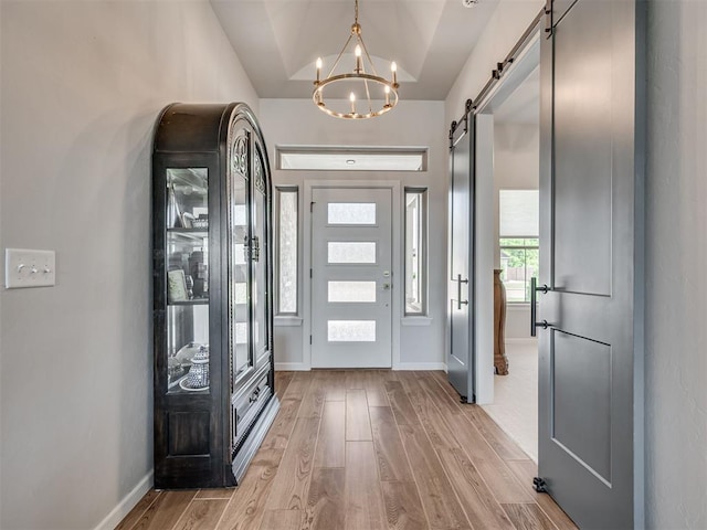 entryway with vaulted ceiling, a barn door, baseboards, light wood finished floors, and an inviting chandelier