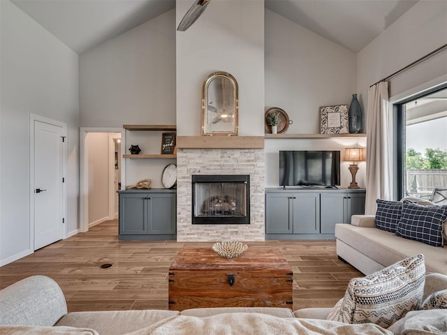 living area with baseboards, high vaulted ceiling, light wood-style flooring, and a fireplace