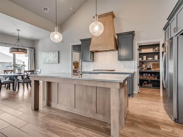 kitchen with a kitchen island with sink, visible vents, light wood-type flooring, high vaulted ceiling, and stainless steel appliances