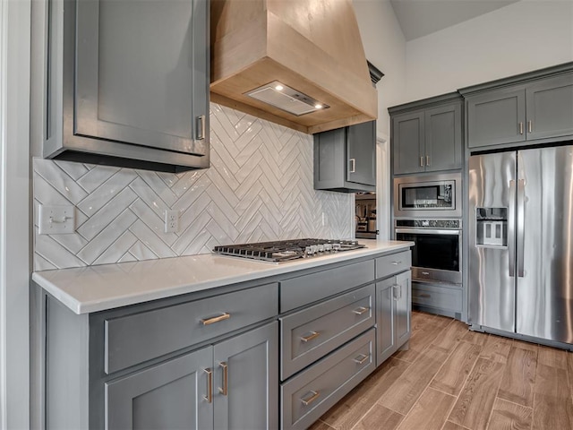 kitchen with light countertops, gray cabinetry, appliances with stainless steel finishes, and custom exhaust hood