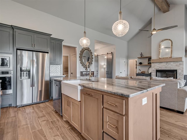 kitchen with light stone countertops, appliances with stainless steel finishes, a barn door, a sink, and beamed ceiling