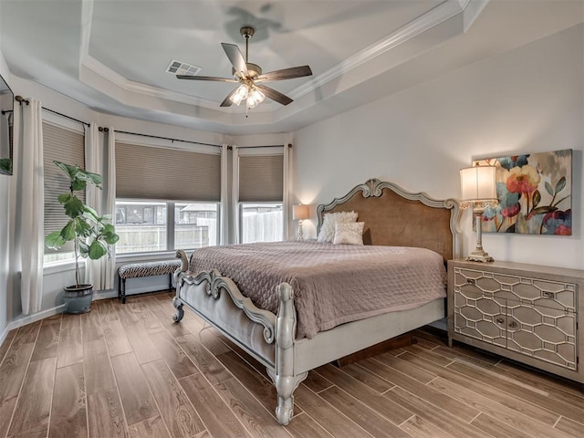 bedroom featuring a raised ceiling, multiple windows, ornamental molding, and wood finished floors
