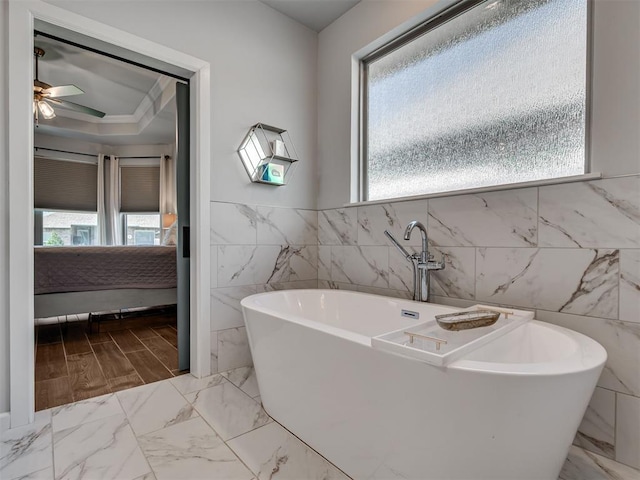 ensuite bathroom featuring marble finish floor, a freestanding tub, tile walls, connected bathroom, and a ceiling fan