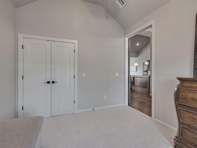 unfurnished bedroom with baseboards, wood finished floors, lofted ceiling, visible vents, and a closet