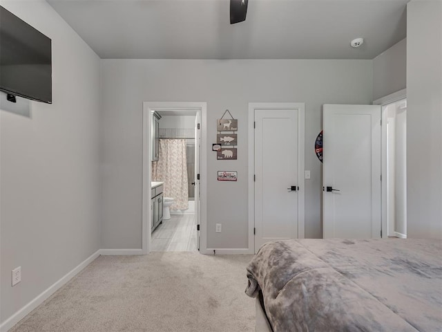 bedroom with baseboards, light colored carpet, ceiling fan, and ensuite bath