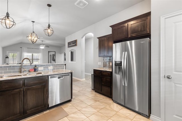 kitchen featuring dark brown cabinetry, appliances with stainless steel finishes, light stone counters, a sink, and arched walkways