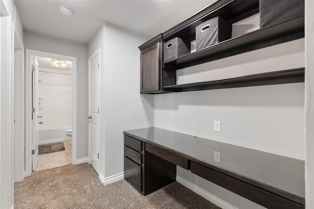 unfurnished office with baseboards, light colored carpet, and built in desk