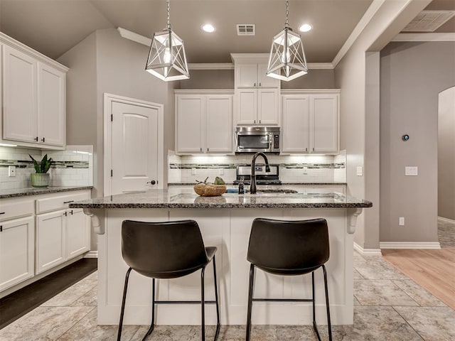 kitchen featuring decorative backsplash, a breakfast bar area, visible vents, stainless steel microwave, and dark stone counters