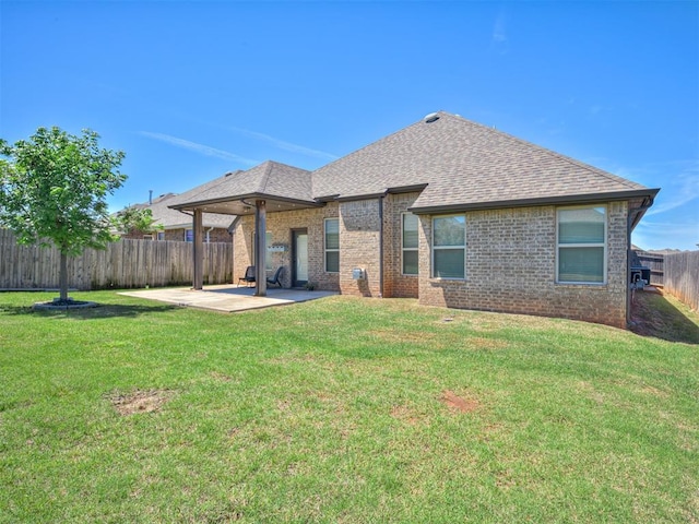 rear view of house featuring roof with shingles, brick siding, a fenced backyard, a patio, and a yard