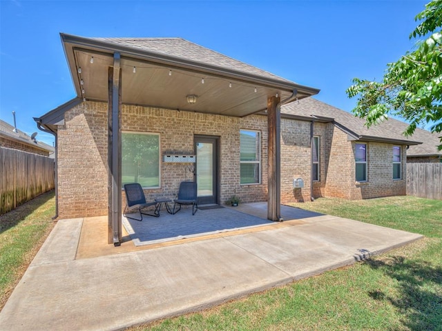 rear view of property with a fenced backyard, roof with shingles, brick siding, a patio area, and a lawn