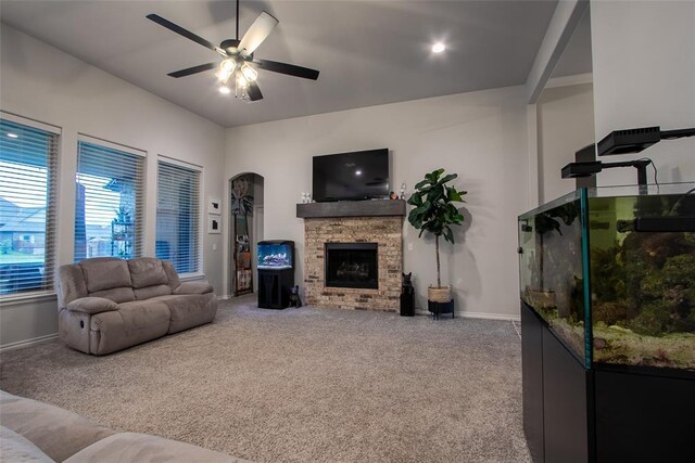 carpeted living room with a ceiling fan, baseboards, a fireplace, and arched walkways