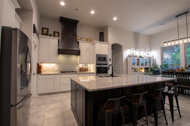 kitchen featuring appliances with stainless steel finishes, premium range hood, a sink, decorative backsplash, and white cabinets