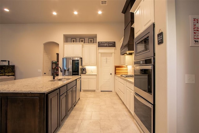 kitchen featuring a sink, stainless steel appliances, white cabinets, a kitchen island with sink, and light stone countertops