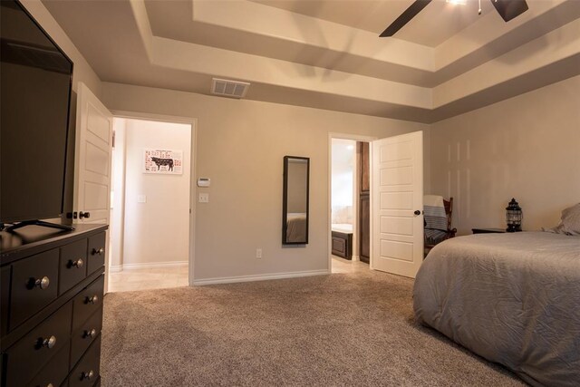 bedroom with a tray ceiling, light colored carpet, baseboards, ceiling fan, and connected bathroom