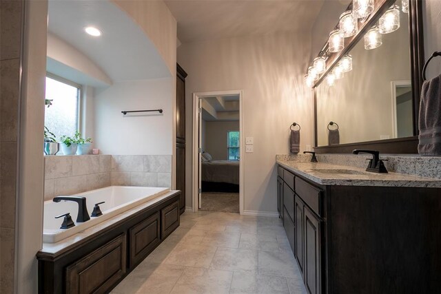 ensuite bathroom featuring a garden tub, double vanity, and baseboards