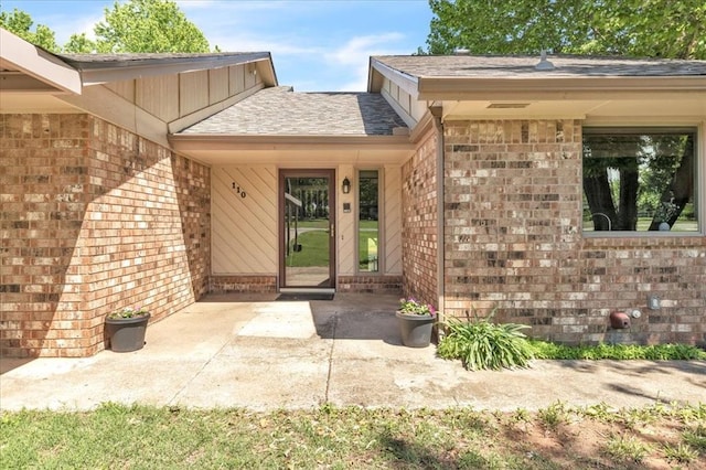 doorway to property with brick siding and roof with shingles