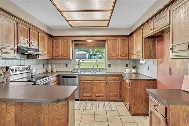 kitchen with brown cabinets, a sink, a peninsula, under cabinet range hood, and stainless steel appliances