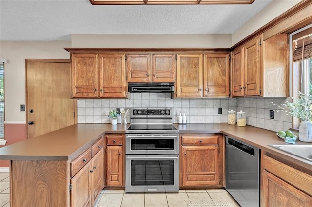 kitchen with brown cabinets, stainless steel appliances, a peninsula, and light tile patterned flooring