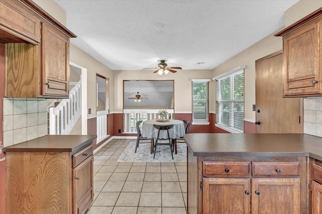 kitchen with ceiling fan, decorative backsplash, dark countertops, light tile patterned floors, and a peninsula