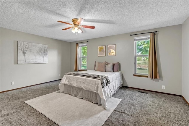 carpeted bedroom featuring a textured ceiling, visible vents, multiple windows, and baseboards