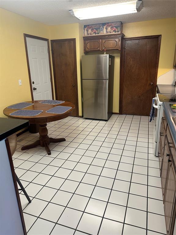 1721 E Ridgeview Ter, Mustang, OK 73064 - kitchen featuring electric range, dark brown cabinetry, a textured ceiling, freestanding refrigerator, and light tile patterned floors