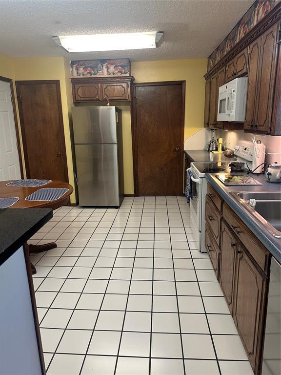 1721 E Ridgeview Ter, Mustang, OK 73064 - kitchen with a sink, a textured ceiling, dark brown cabinetry, and white appliances