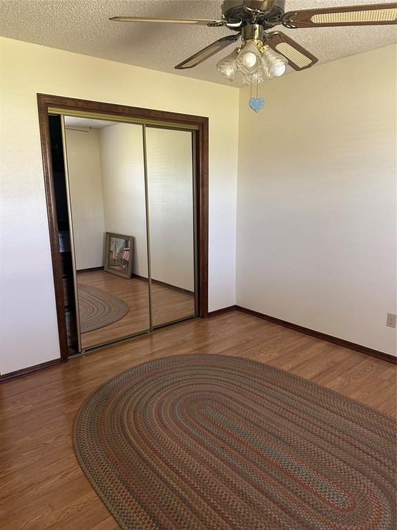 1721 E Ridgeview Ter, Mustang, OK 73064 - unfurnished bedroom with a closet, wood finished floors, baseboards, ceiling fan, and a textured ceiling