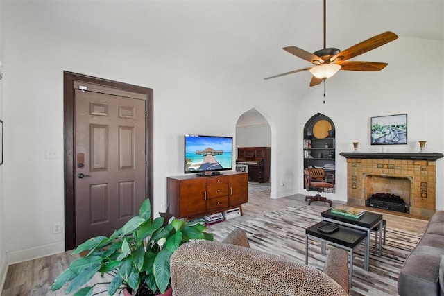1912 NW 22nd St, Oklahoma City, OK 73106 - living room featuring built in shelves, arched walkways, ceiling fan, a tiled fireplace, and light wood-style floors