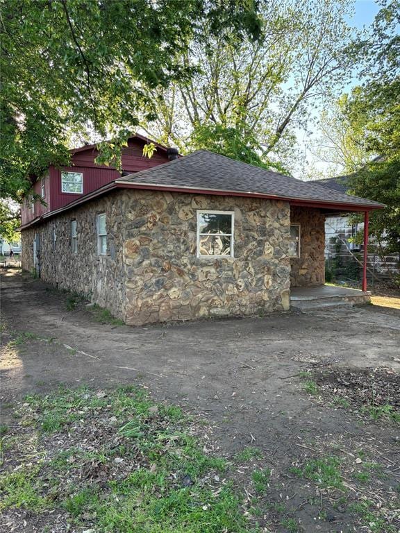 view of property exterior with roof with shingles and stone siding
