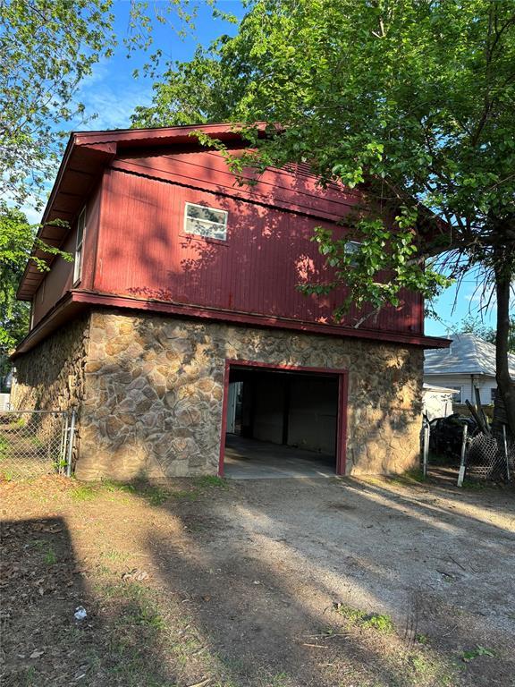 view of home's exterior featuring fence, stone siding, a barn, an attached garage, and driveway