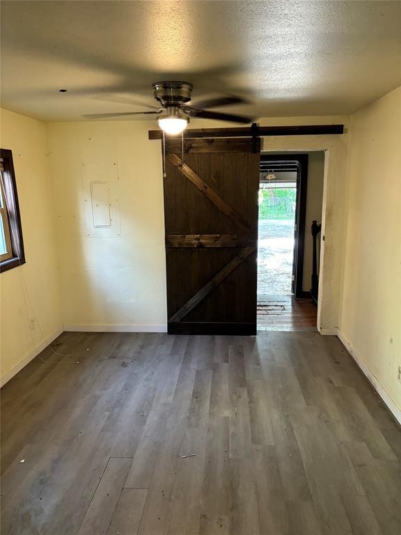 empty room featuring baseboards, ceiling fan, a barn door, and wood finished floors