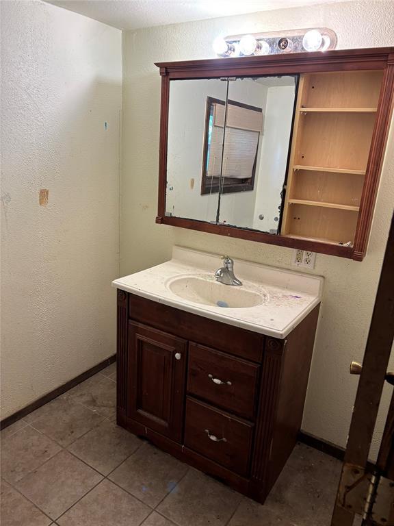 bathroom with vanity, baseboards, a textured wall, and tile patterned floors