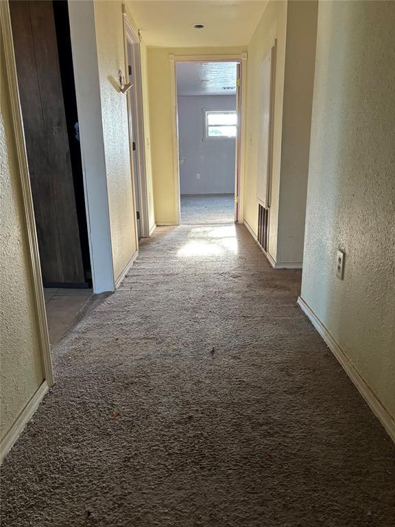 hallway with carpet floors, a textured wall, and baseboards