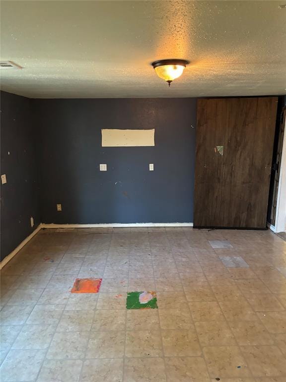 empty room featuring visible vents, a textured ceiling, and baseboards